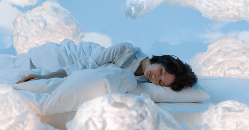 Ženska v globokem spancu sredi oblakov, ki ponazarja bizarne sanje po jemanju magnezija in vitaminov.